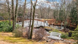 Un pont en bois reliant deux parties d’un terrain, ceinturé d’arbres et bordé d’un petit étang.