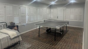 Een kamer met een tafeltennistafel, een bed en een raam met jaloezieën.