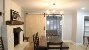 Een eetgedeelte met een houten tafel en stoelen, een metselwerk open haard en een kroonluchter.
