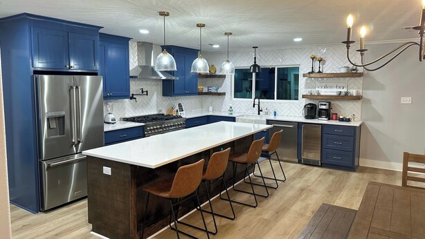 Een moderne keuken met blauwe kastjes, een roestvrijstalen koelkast, een centraal eiland met barkrukken, hanglampen en een koffiehoek.