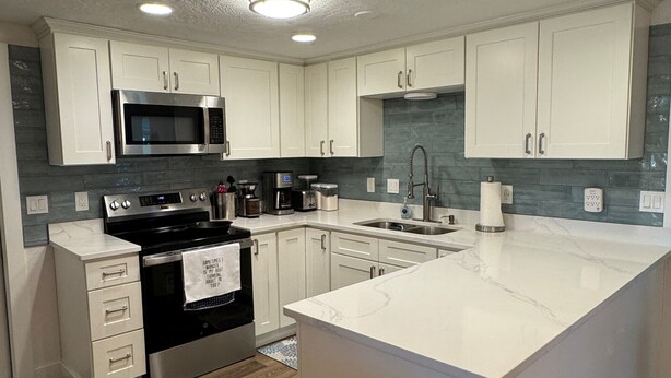 A modern kitchen with white cabinets, a central island, stainless steel appliances, and a backsplash with blue tiles. - Gulfside Getaway - Newly renovated waterfront 3-bedroom w/dock in Port Richey (Port Richey)