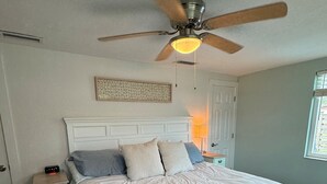 A bedroom with a bed, a nightstand, a ceiling fan, a wall-mounted light, a door, and a window. - Gulfside Getaway - Newly renovated waterfront 3-bedroom w/dock in Port Richey (Port Richey)