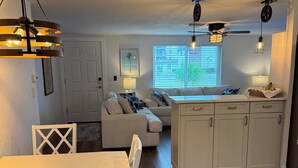 A modern kitchen with white cabinetry, a dining area with a white table and chairs, and a cozy seating area with a sofa and cushions. - Gulfside Getaway - Newly renovated waterfront 3-bedroom w/dock in Port Richey (Port Richey)