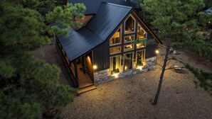 Une cabane dotée d’un toit en pente, de grandes fenêtres et de fondations en pierre, le tout entouré de pins.