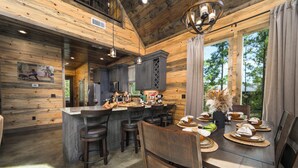 L’intérieur d’un chalet en bois comprend une cuisine et un coin repas, avec un grand îlot central, des tabourets de bar et une vue sur l’extérieur.