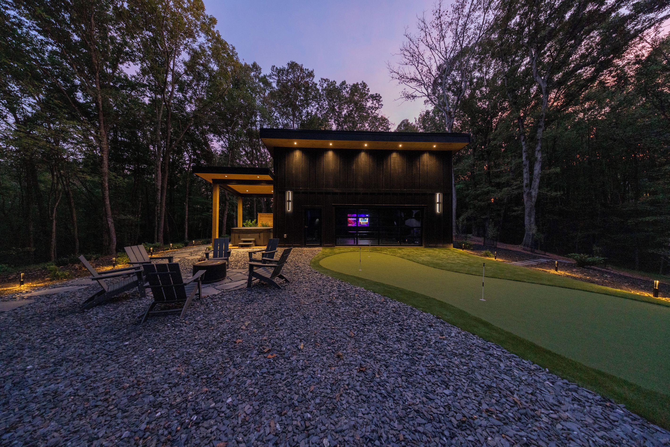 A modern outdoor entertainment area with a flat-screen TV, seating, and a well-maintained lawn.