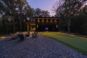 A modern outdoor entertainment area with a flat-screen TV, seating, and a well-maintained lawn.