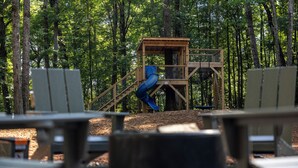 A playground with a blue slide and a wooden play structure in a forested area.