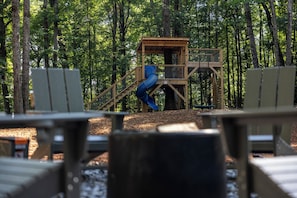 A playground with a blue slide and a wooden play structure in a forested area.