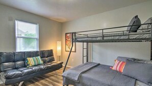 A compact room with a bunk bed, a leather sofa, and a window with blinds.