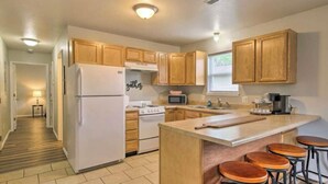 A modern kitchen with wooden cabinets, a refrigerator, stove, microwave, and bar stools.