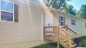A single-story mobile home with a wooden porch and a small staircase leading to a front door.