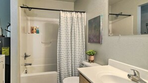 A bathroom with a bathtub, shower curtain, toilet, sink, and a small potted plant.