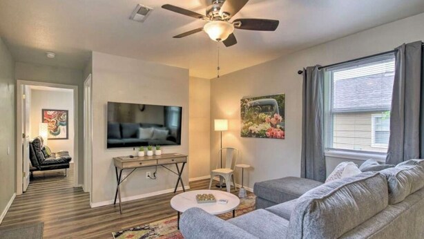 A modern living room with a ceiling fan, a flat-screen TV, a sofa, a coffee table, and a window with curtains.