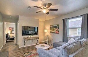 A modern living room with a ceiling fan, a flat-screen TV, a sofa, a coffee table, and a window with curtains. - Pet-Friendly West Plains Home Near Downtown!
 (West Plains)