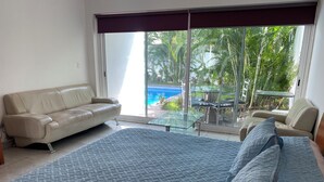 En rummelig opholdsstue med en stor seng, en beige sofa og et glasbord.