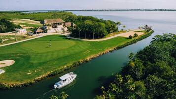 A golf course with a water body, a boat, and a building with a thatched roof.