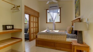 Un dormitorio con cama, mesita de noche de madera, radio, ventilador de techo y ventana con cortina.