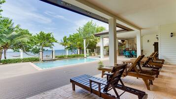 A poolside area with lounge chairs, a small table, and a thatched-roof structure.
