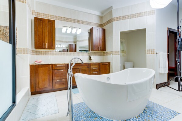 A modern bathroom with a freestanding bathtub, wooden cabinets, and a tiled backsplash.