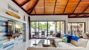Amplia sala de estar con televisor grande, techo de madera y vista al patio exterior.