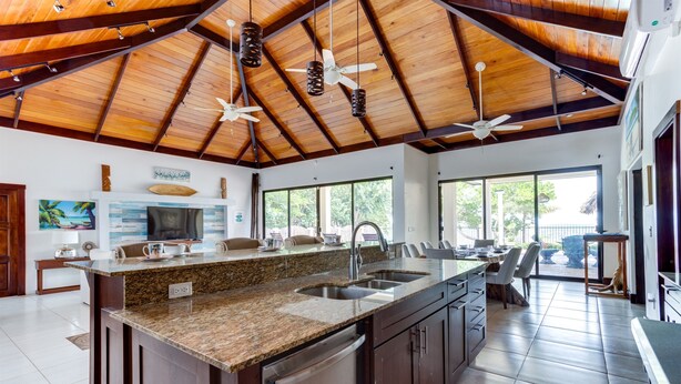 Una cocina amplia con una isla grande, encimera de granito y electrodomésticos de acero inoxidable. Hay ventiladores de techo, ventanas grandes y vistas al exterior.