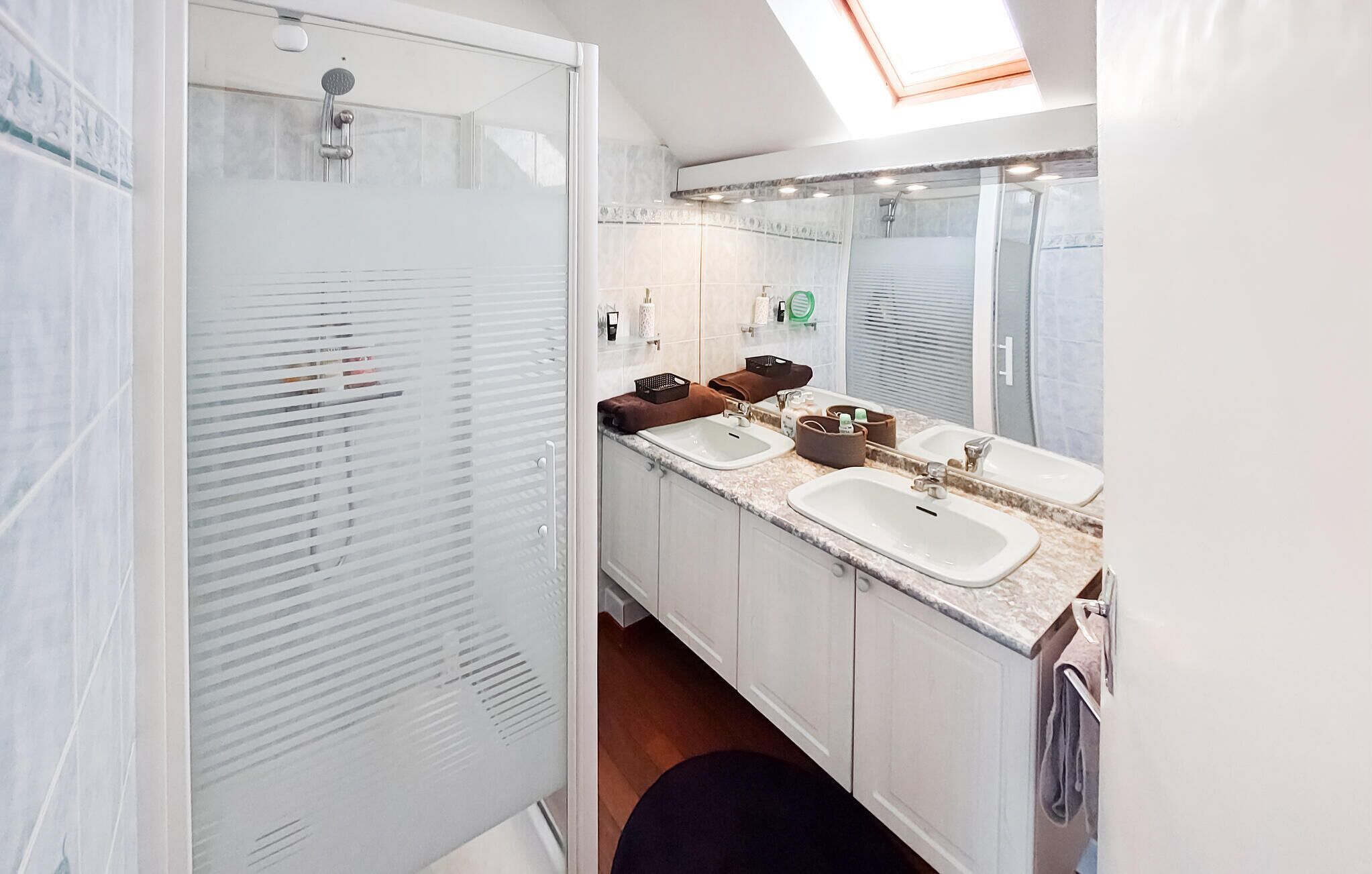 A modern bathroom with two sinks, a shower, and a skylight.