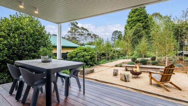 An outdoor patio with a wooden table and chairs, a fire pit, and a view of a green landscape.
