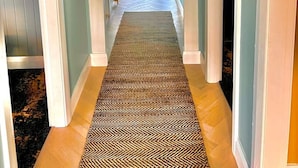 A hallway with a patterned rug, white trim, and a view into another room.