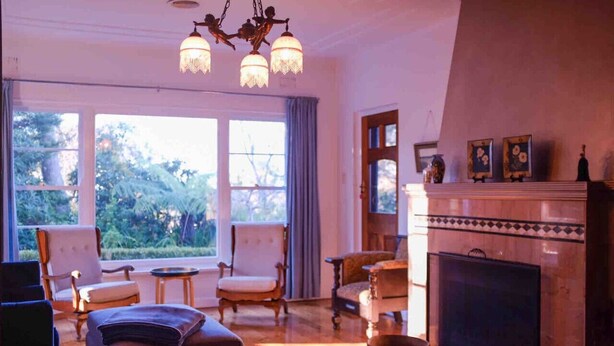 A spacious living room with a fireplace, large windows, and a chandelier. - Sublime Art Deco Cottage: Leura, Blue Mountains (Leura)