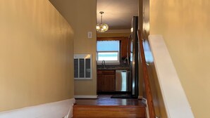 Eine Treppe mit Holzboden und weißen Geländern führt zu einer Küche mit Holzschränken und einem Edelstahlkühlschrank.