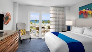 Habitación de hotel con cama, una silla, un escritorio y vista a la playa y al océano.