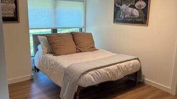 A bedroom with a bed, a ceiling fan, a window with blinds, and a painting on the wall.