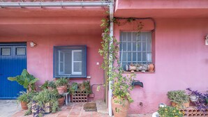 A pink building with a blue door, a window with a screen, and various potted plants on the ground and on the windowsill. - Cozy home in Sant Miquel de Fluvià (Sant Miquel de Fluvià)