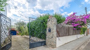A gated entrance with a stone wall and a blue door, surrounded by lush greenery and flowering plants. - Cozy home in Sant Miquel de Fluvià (Sant Miquel de Fluvià)