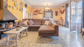 A cozy living room with a brown sofa, a wooden coffee table, and a fireplace. There are decorative plates on the wall and a large window with curtains. - Cozy home in Sant Miquel de Fluvià (Sant Miquel de Fluvià)