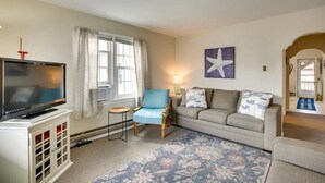 Una sala de estar con televisor, un sillón azul, un sofá gris y una decoración de estrella de mar en la pared.