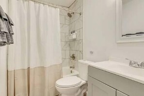 A bathroom with a toilet, a glass shower enclosure, and a white sink with a mirror above it. - Spacious 3 Bedroom in midtown Mobile, AL (Mobile)