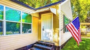 Una casa con puerta principal, un conjunto de escalones que la conducen y una bandera estadounidense a la derecha.