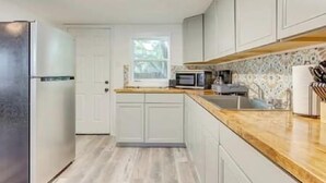 Una cocina moderna con armarios blancos, un refrigerador de acero inoxidable, un microondas y una encimera de madera.