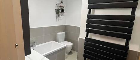 A bathroom with a white sink, a bathtub, a toilet, and a black towel rack.