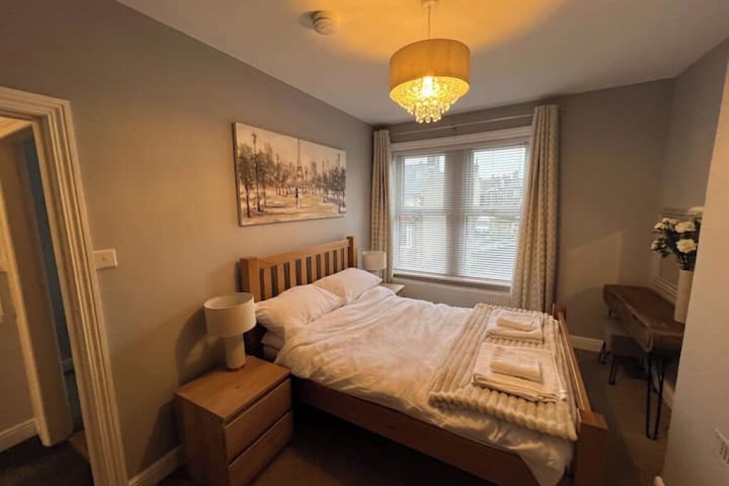 Un dormitorio ordenado con cama, mesita de noche, lámpara y un cuadro en la pared.