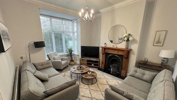 Ein Wohnzimmer mit zwei grauen Sofas, einem Fernseher, einem Kamin und einer Chandelier.