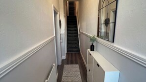Ein schmaler Flur mit Treppe, Heizkörper, Teppich mit Muster, einem weißen Schrank und einem Spiegel an der Wand.