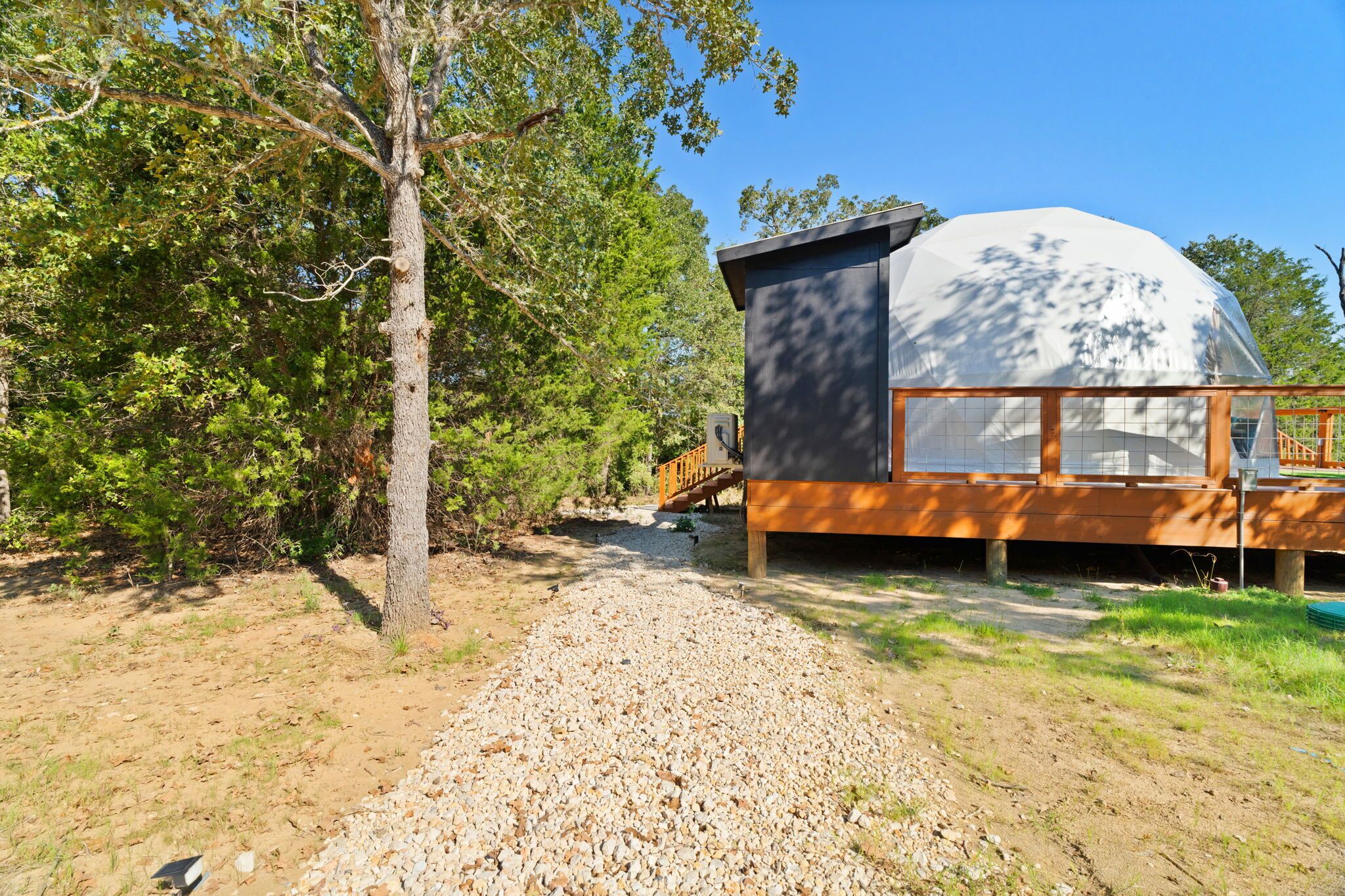 A modern house with a large dome structure, surrounded by trees and a gravel path.