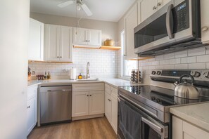 Une cuisine moderne avec des meubles blancs, des appareils électroménagers en acier inoxydable, un lave-vaisselle et un four à micro-ondes.