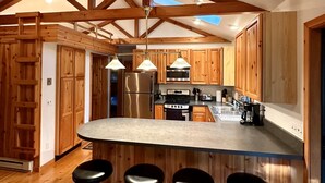 A spacious kitchen with wooden cabinets, a central island with bar stools, and a skylight. - Riverside Cabin Near Torch Lake – Kayaks Included! (Rapid City)