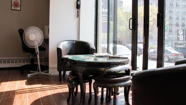 Een kamer met een glazen tafel, een stoel, een ventilator en uitzicht op de straat.