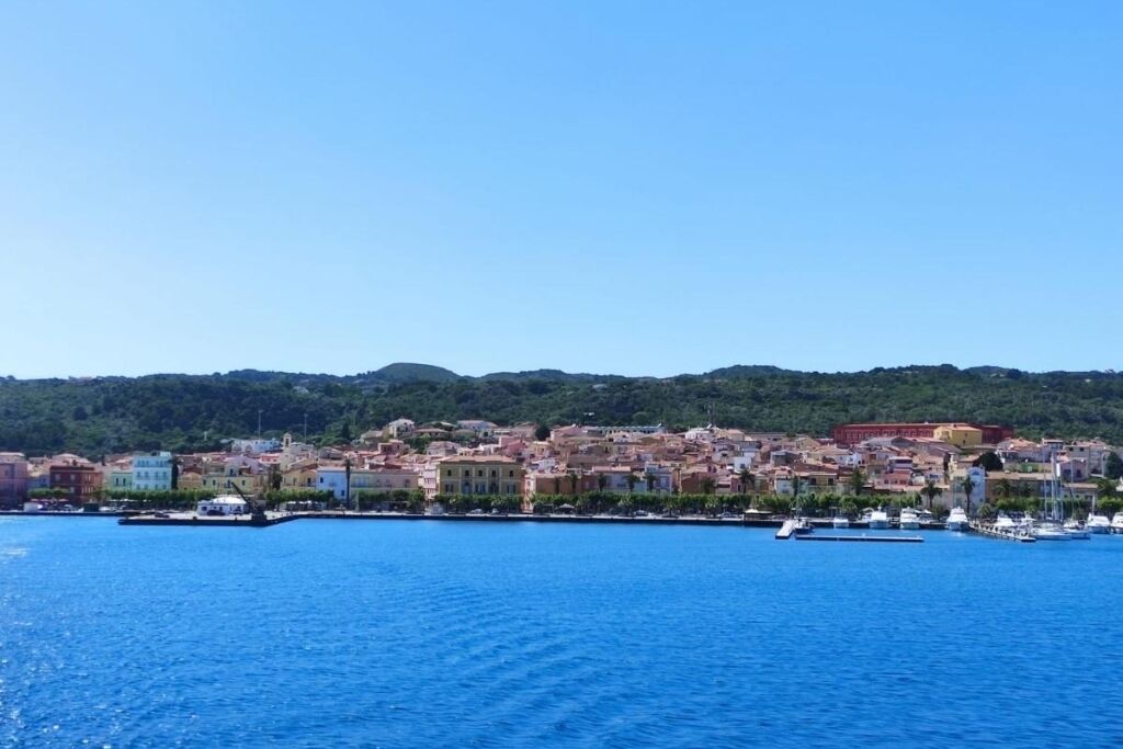 Une ville côtière aux bâtiments aux couleurs vives, qui s’étend le long du front de mer, avec un port de plaisance rempli de bateaux et des collines en arrière-plan.