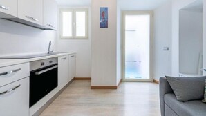 A modern kitchen with white cabinets, a built-in oven, and a window. - Apartments La perla - Apartment with Balcony (Carloforte)